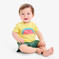A baby sitting upright on the ground wearing a watermelon graphic t-shirt
