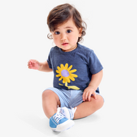 A baby sitting upright on the ground wearing a sunflower graphic t-shirt
