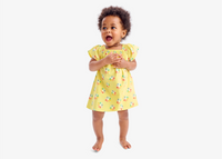 A young baby standing and clapping their hands wearing our new yellow rainbow sun dress.
