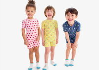 3 kids standing in a row laughing and smiling, wearing our new spring PJs in ladybug, suns, and lightning bolts. 