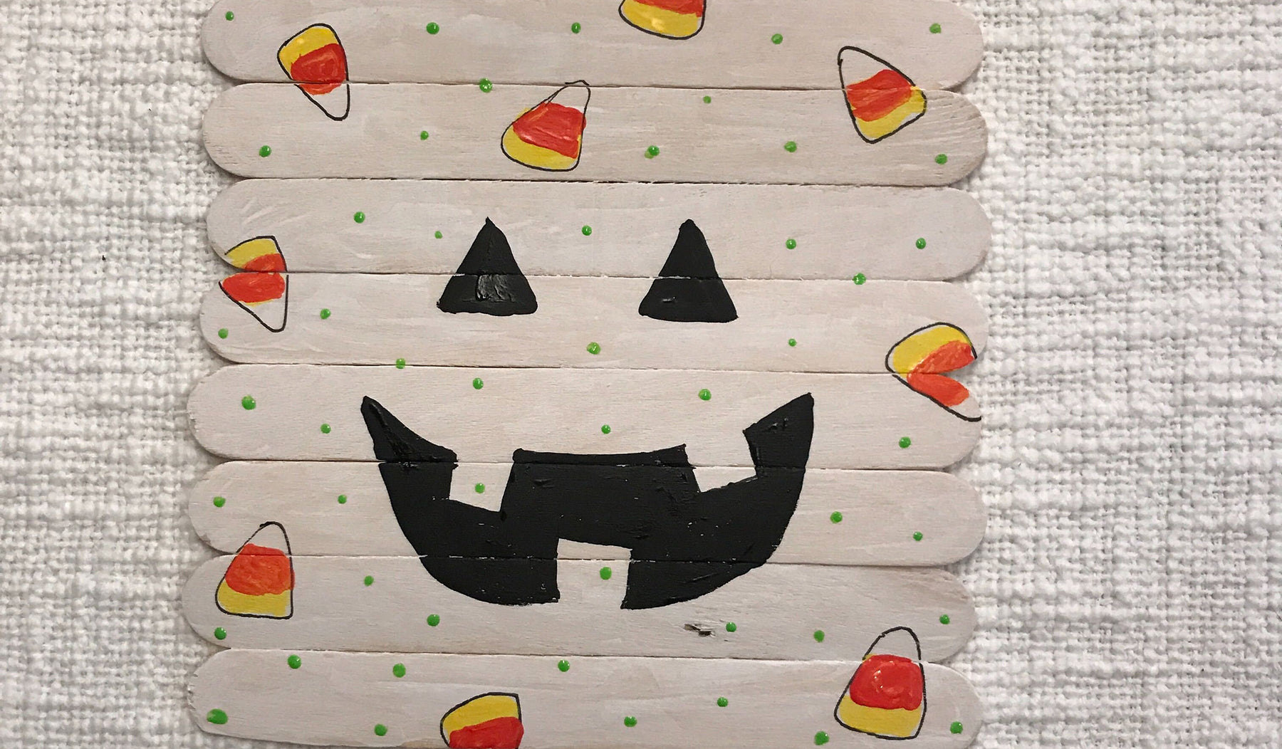 Popsicle sticks painted to form a square puzzle with a Jack O' Lantern face with candy-corn designs on top.