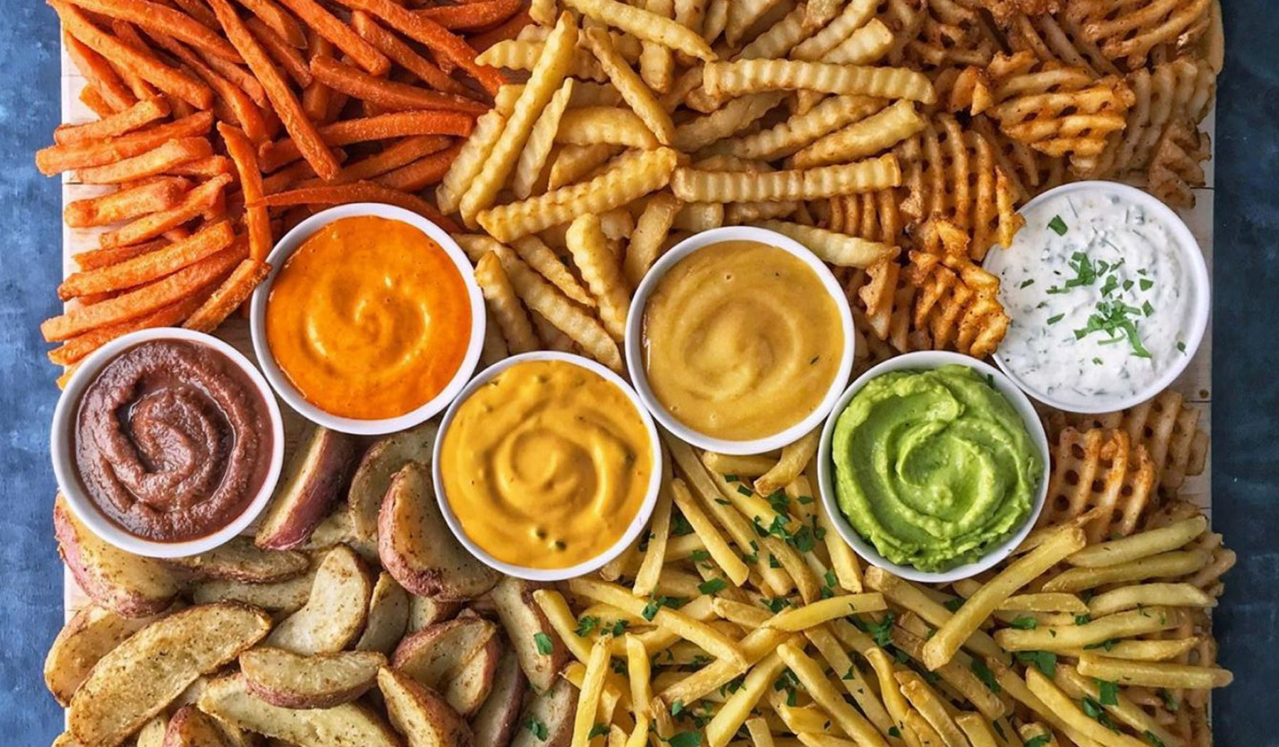 Different kids of french fries on a platter with dipping sauces 