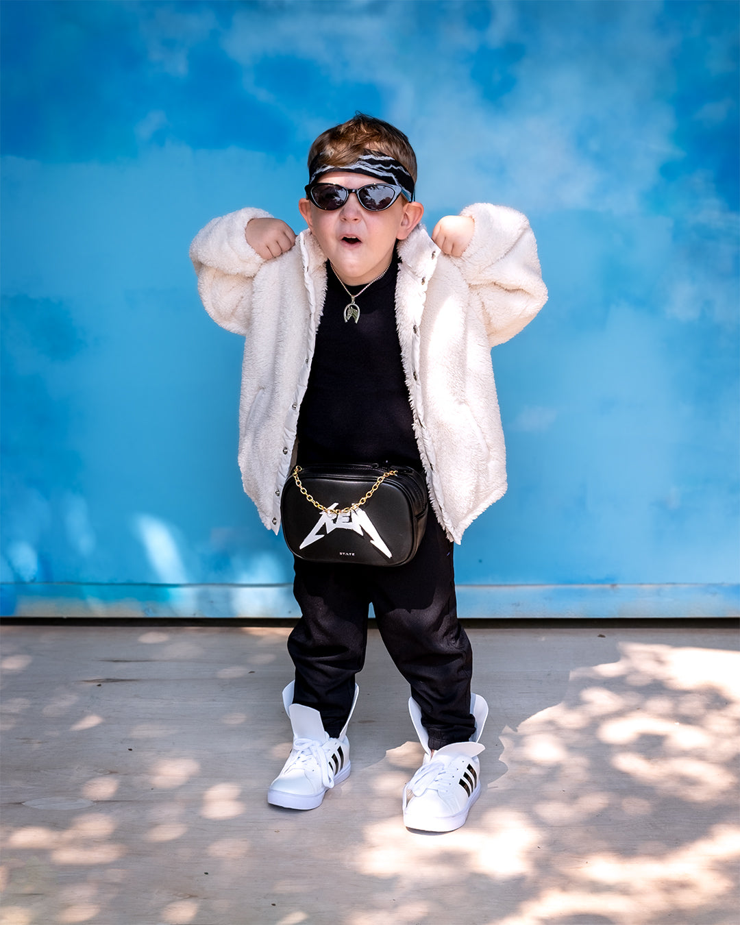 Mojo Dojo Casa House Ken (Barbie Movie): One child wearing a black outfit with a cream coat over top, a black fanny pack, black sunglasses, and black headband.