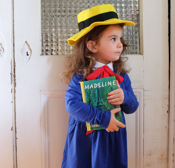Madeline (Kid): A child wearing a yellow hat, blue dress layered over a white top, with a red bow around the neck.