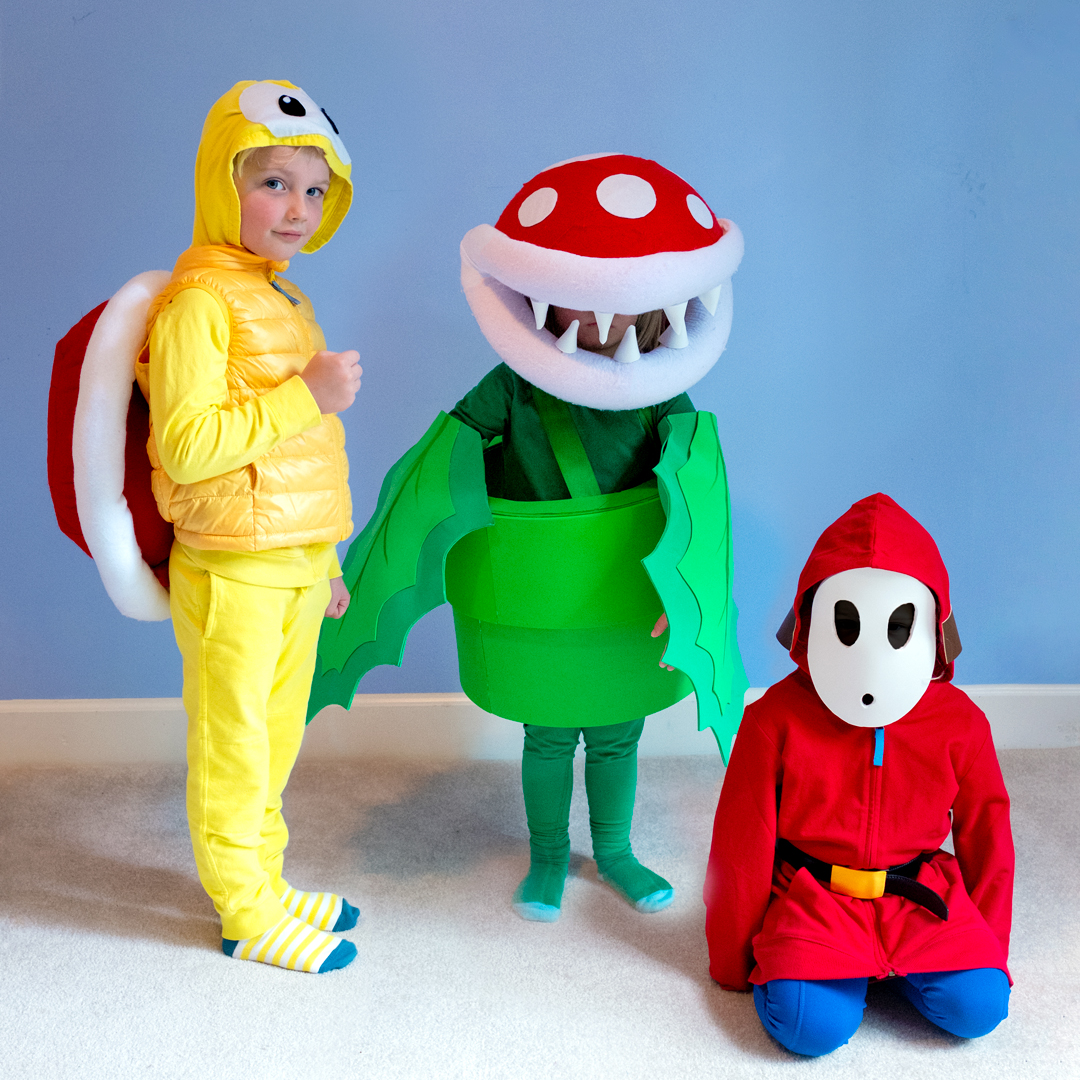 The Mario Villains Squad consists of three children in Mario-themed costumes. One is dressed as Koopa Troopa in yellow, another as Piranha Plant in green, and the third as Shy Guy in red and blue.
