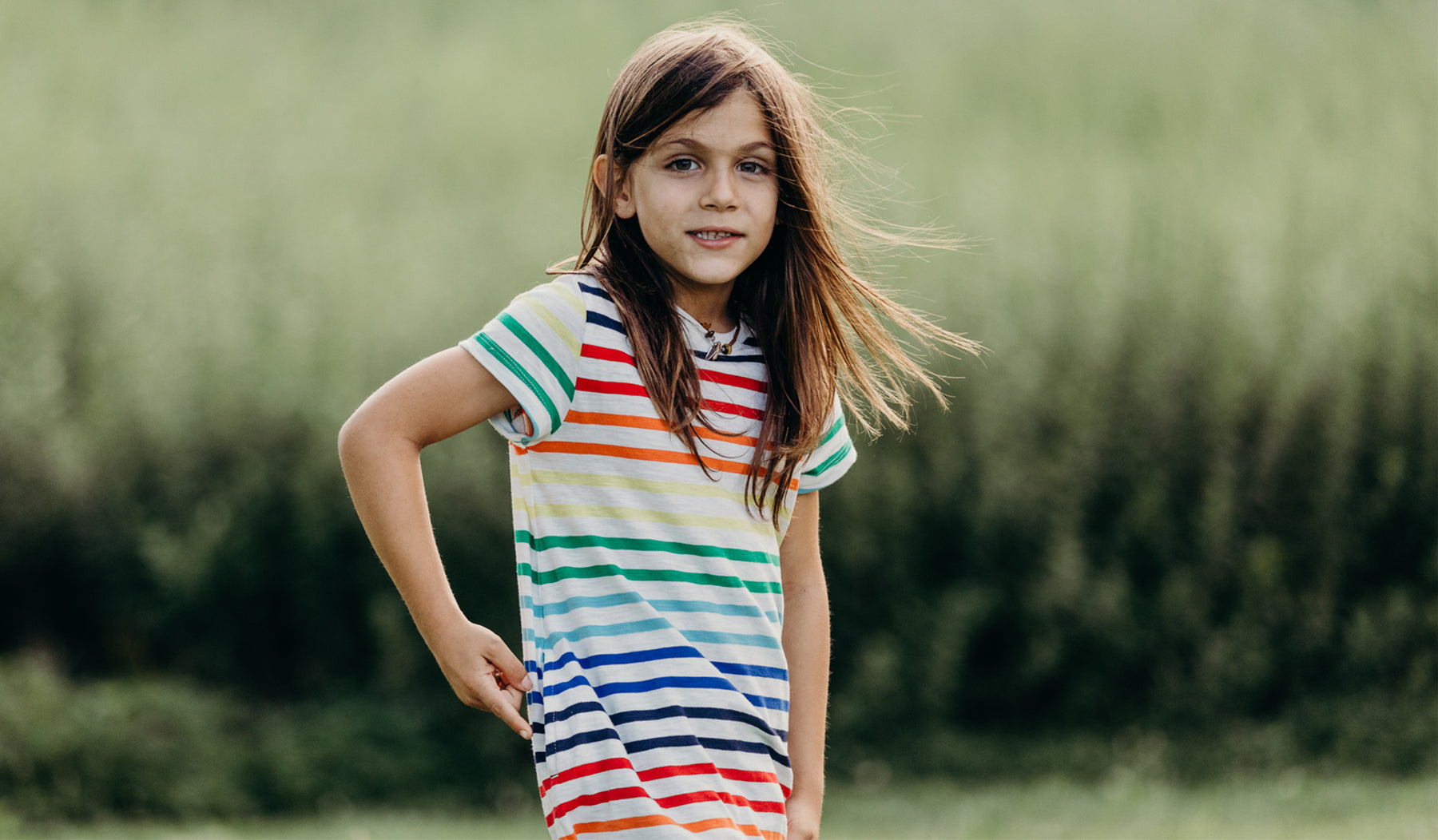 little boy with long hair wears primary kids rainbow stripe t shirt dress