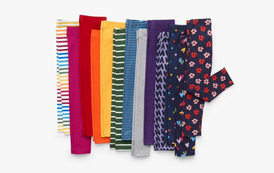 Ten pairs of kids leggings laid flat next to each other and arranged in rainbow order to show solid colors, patterns and stripes.