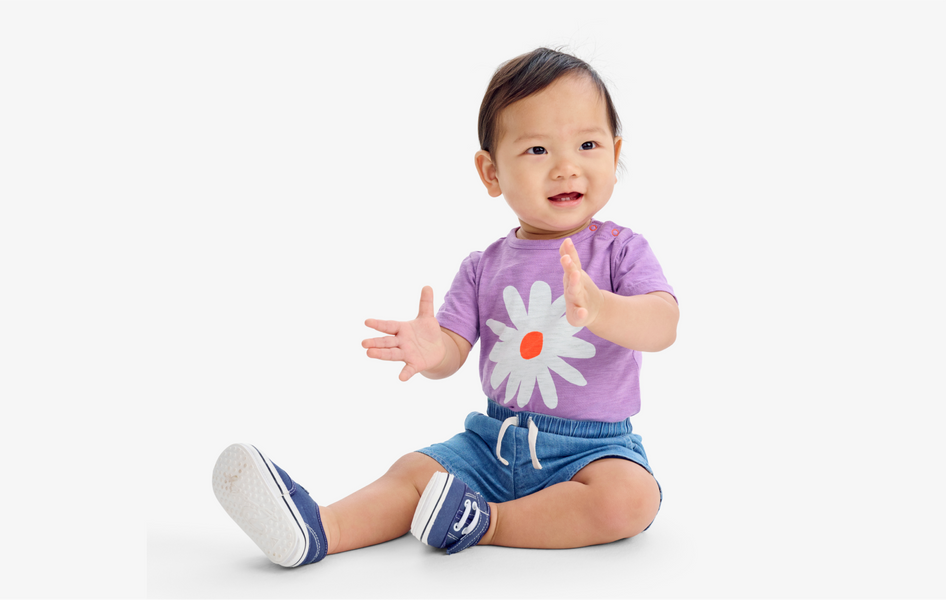A baby sitting up straight clapping their hands wearing our daisy bodysuit.