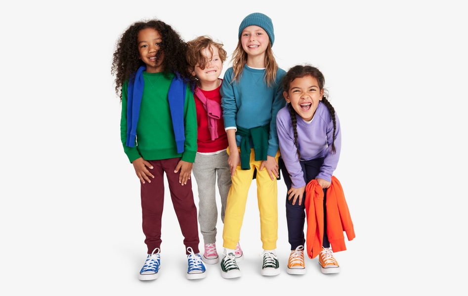 4 kids standing side by side wearing colorful cozy fall clothing, including sweatshirts, sweatpants, leggings, and t-shirts.