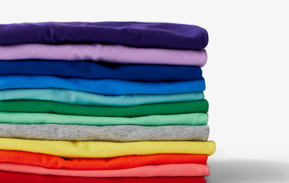 A close up image of children's clothing folded and stacked in a pile in rainbow order.