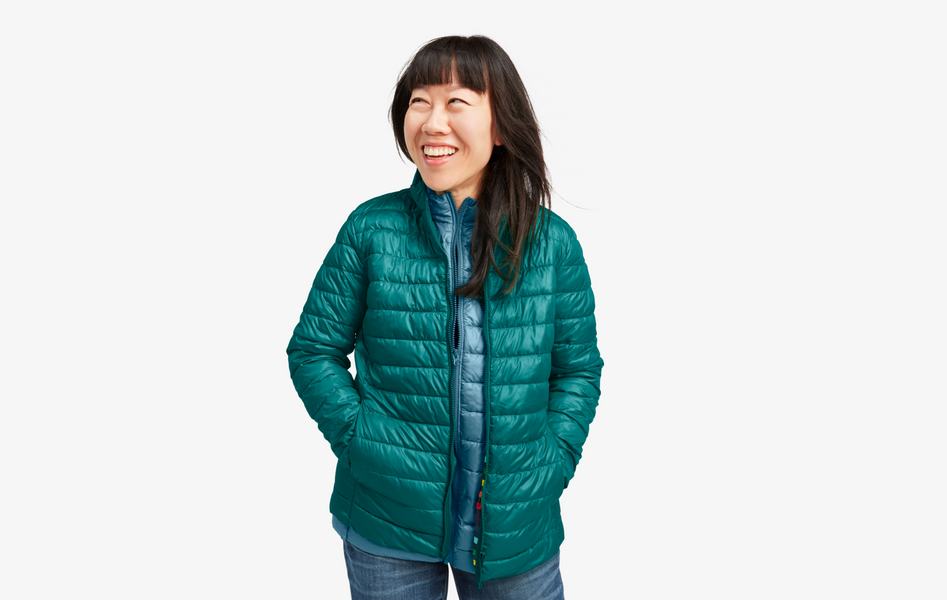 An adult wearing a slate blue lightweight puffer jacket with her hands in the pockets.