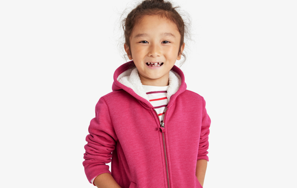 A young child wearing a pomegranate color zip up hoodie with a cozy fleece lined hood.