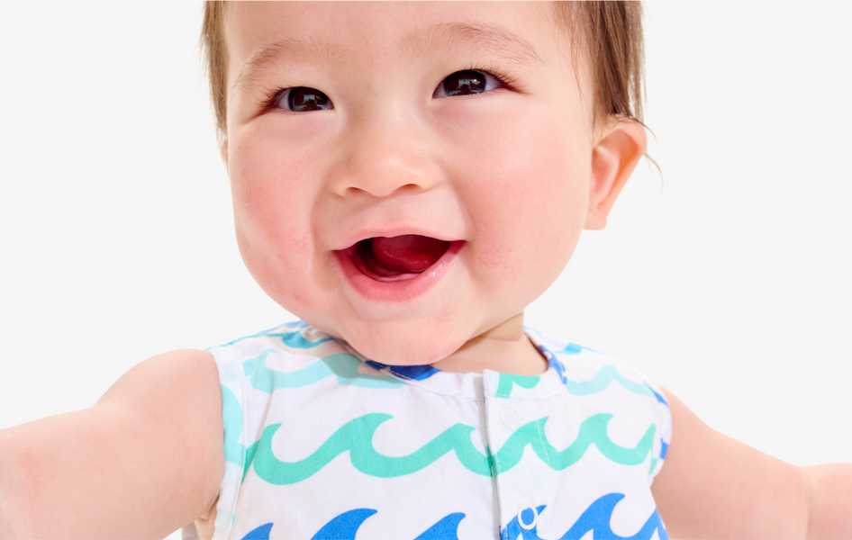A close up image of a baby with their hands wide open smiling at the camera wearing our new sea wave shortie