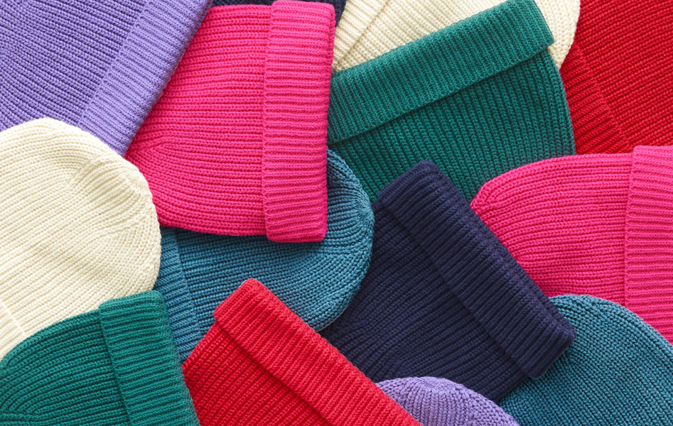 A close-up image of multiple knit beanies scattered in a pile, all in solid colors.