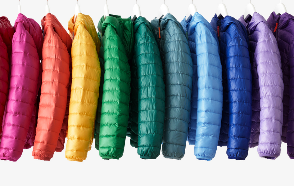 11 lightweight puffer jackets hanging on rack, arranged in rainbow order.