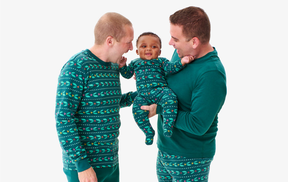 2 fathers holding their baby wearing our mix and match holiday PJs from our spruce collection.
