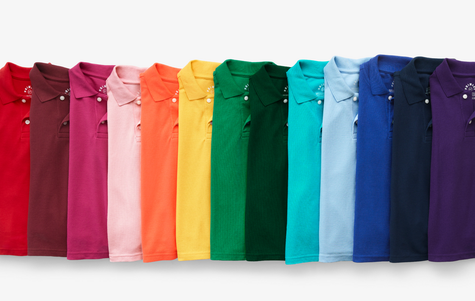 A dozen kids short sleeve collared polo shirts folded up and arranged laying down in a rainbow
