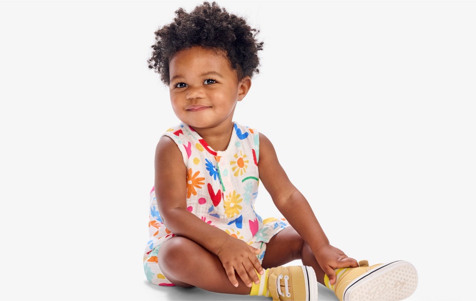 A close-up image of a young baby in a short sleeve romper with a rainbow garden pattern