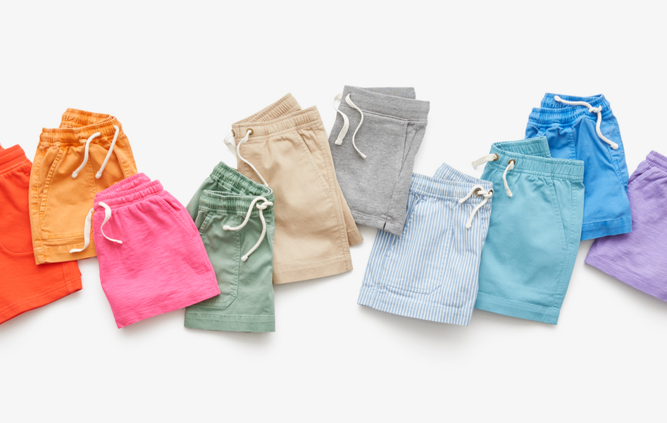 Multiple pairs of kids drawstring shorts, folded and laid flat in a rainbow