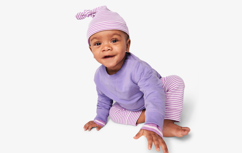 A baby wearing a lavendar and white striped hat, a solid lavendar sweatshirt, and matching lavender and white striped pants.