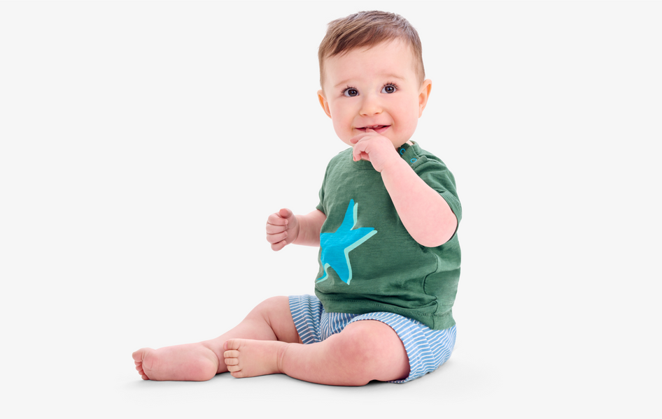 A baby sitting upright wearing a long sleeve light blue t-shirt and navy blue pull-on pants