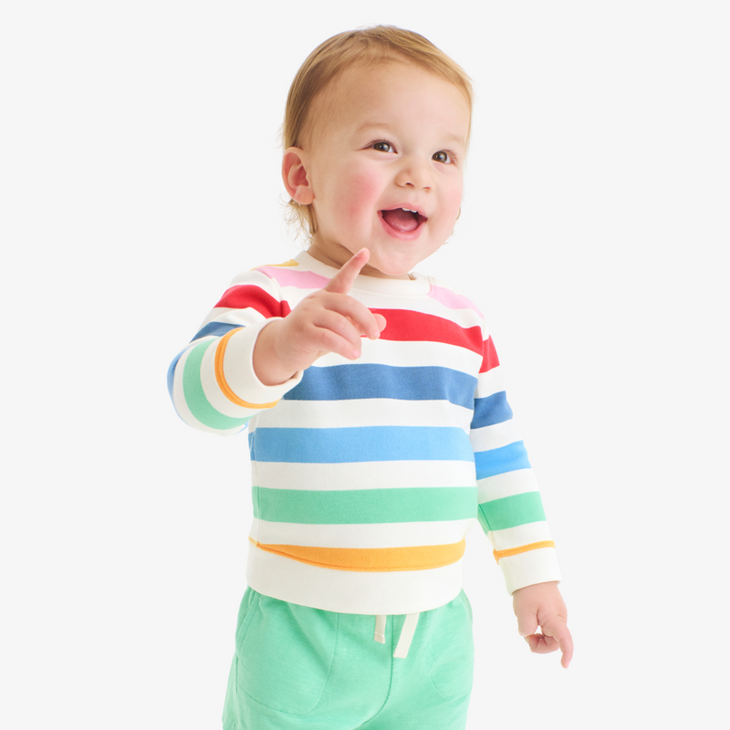 Child wearing a colorful striped sweater and green pants on a white background