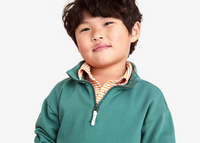A young boy looking at the camera wearing a green quarter zip sweatshirt with a polo under