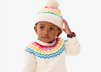 A baby sitting on the ground wearing our fair isle sweater in oat with a matching beanie