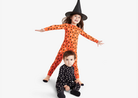 Two children, wearing orange and black Halloween patterned pajamas, with stars moons and witch hats on them