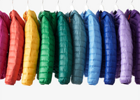 A close-up photograph of a multiple kids' lightweight puffer jackets hanging on a clothing rack in rainbow order