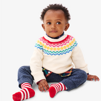 A young baby sitting on the floor wearing our new oat fair isle sweater
