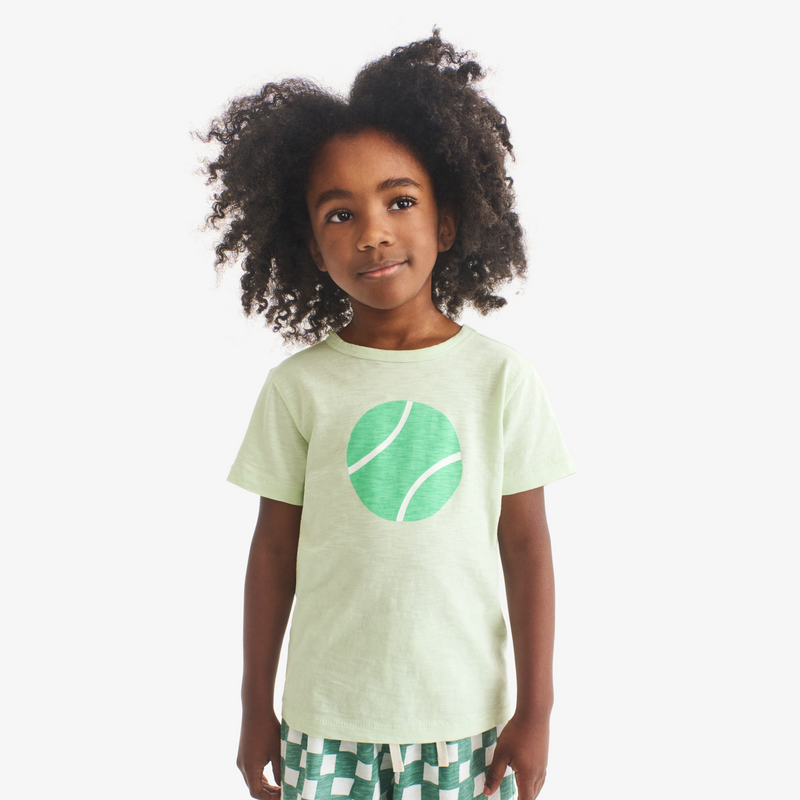 Child wearing a light green t-shirt with a tennis ball graphic on a white background