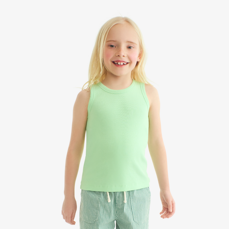 Young girl wearing a light green sleeveless top and striped pants on a white background