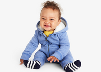 A baby sitting on the ground wearing our new blue zip romper wth teddy fleece lining. 