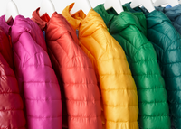 A close-up photograph of a multiple kids' lightweight puffer jackets hanging on a clothing rack in rainbow order