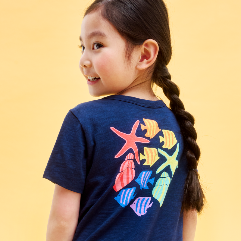 Child wearing a navy blue t-shirt with colorful sea creature designs on a yellow background