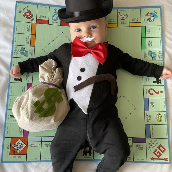 A baby wearing a morning suit with a bowtie and top hat. Under the baby's armpit there is a bag that a dollar sign.