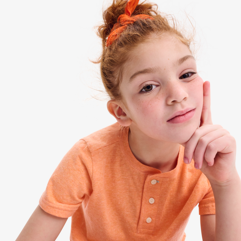 Young girl wearing an orange shirt with a plain background