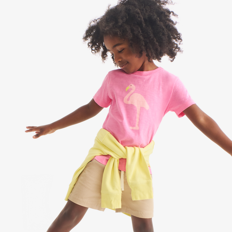 Child wearing a pink shirt with a flamingo design and a yellow and beige skirt on a white background