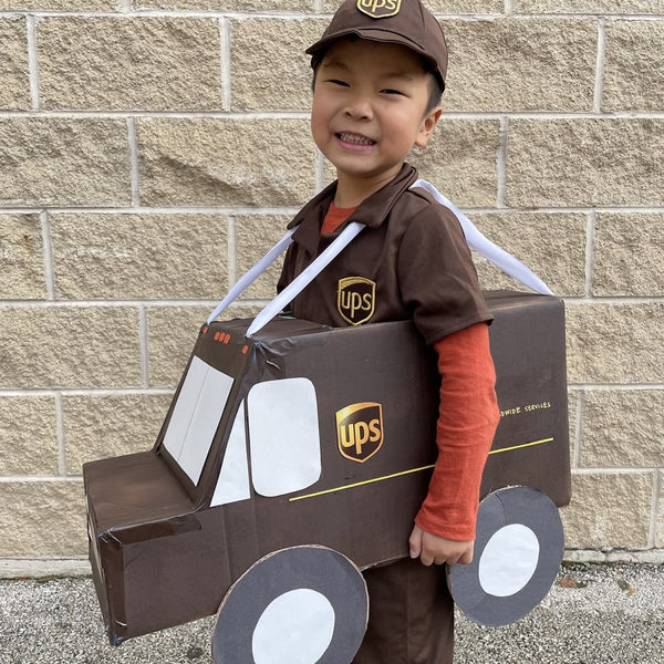 A boy wearing UPS uniform and carrying a cardboard made UPS truck.