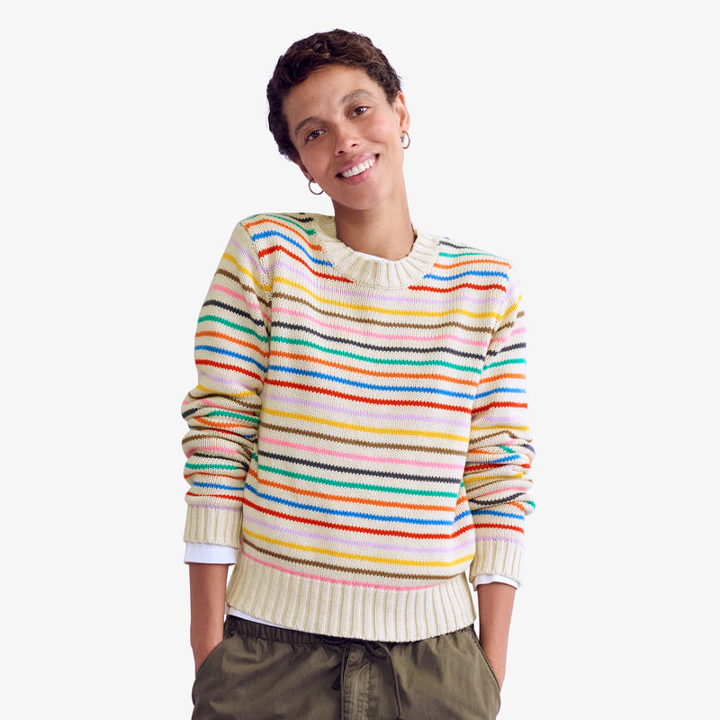 A woman wearing a cream sweater with thin rainbow stripes