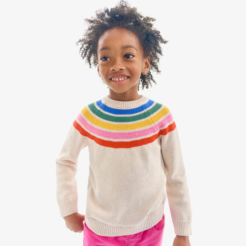 A girl wearing a cream sweater with a rainbow yoke