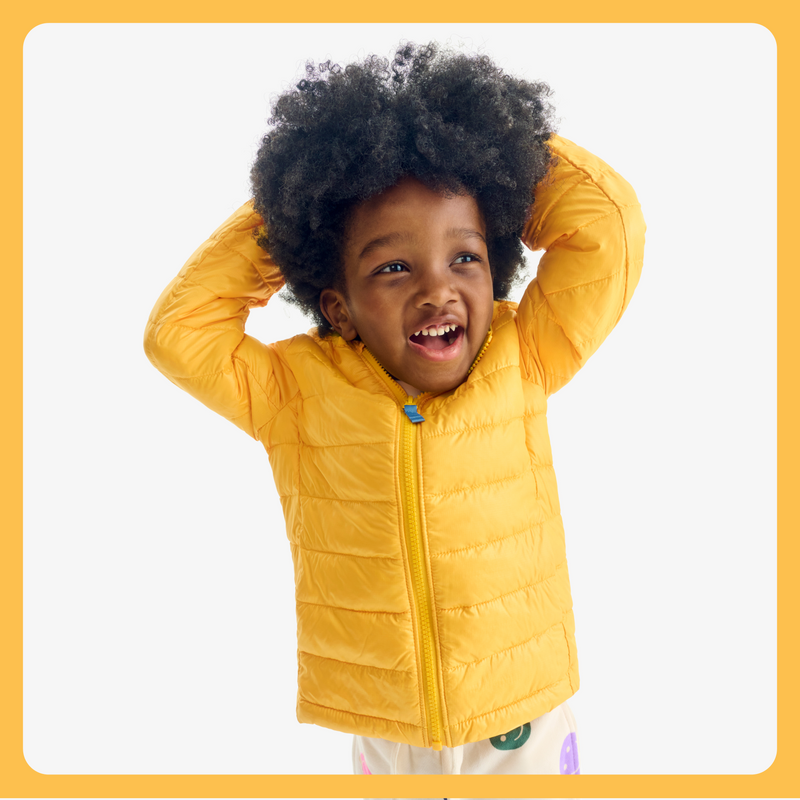 A kid wearing a yellow puffer jacket zipped up with their hands above their head